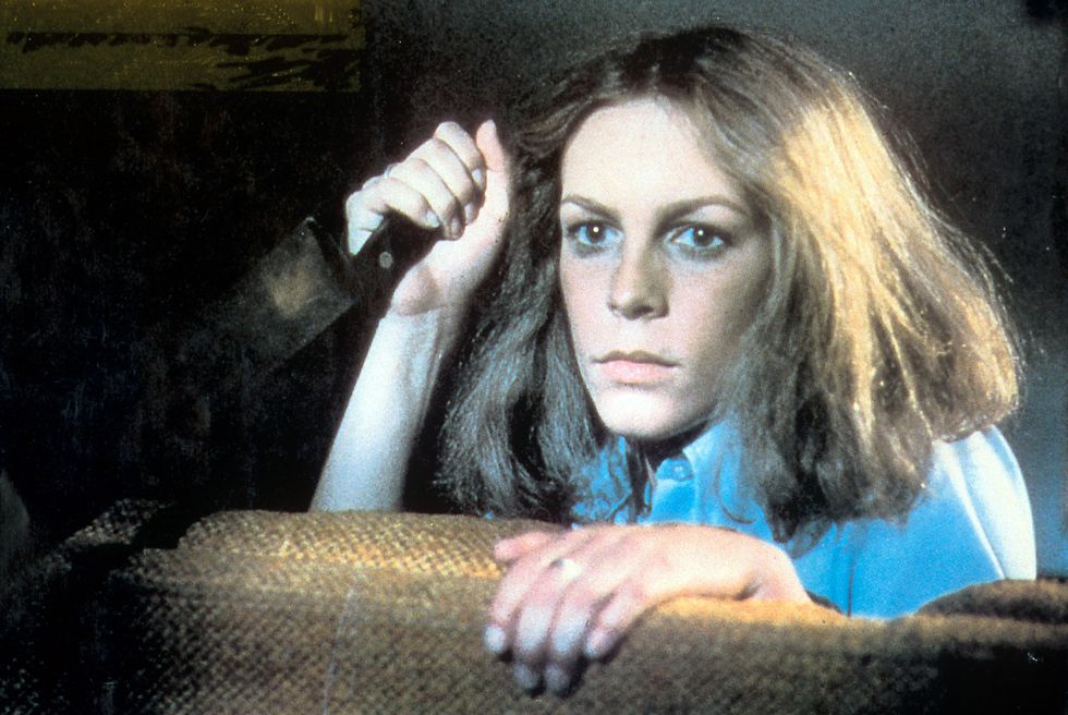 a photo of jamie lee curtis starring in the film halloween, holding a knife and looking over a couch