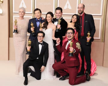 first row shows ke huy quan and daniel kwan kneel holding oscars second row shows jamie lee curtis, james hong, michelle yeoh, jonathan wang, stephanie hsu, and daniel scheinert stand while holding oscars