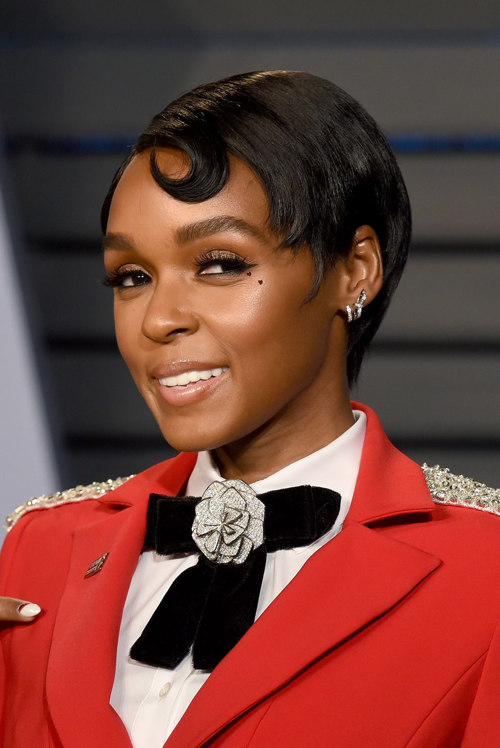 janelle monae in a red blazer with black bow and a slicked down pixie