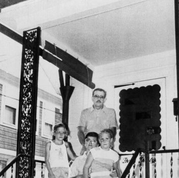 two young girls and their parents sit and stand on the porch of a house right outside the front door