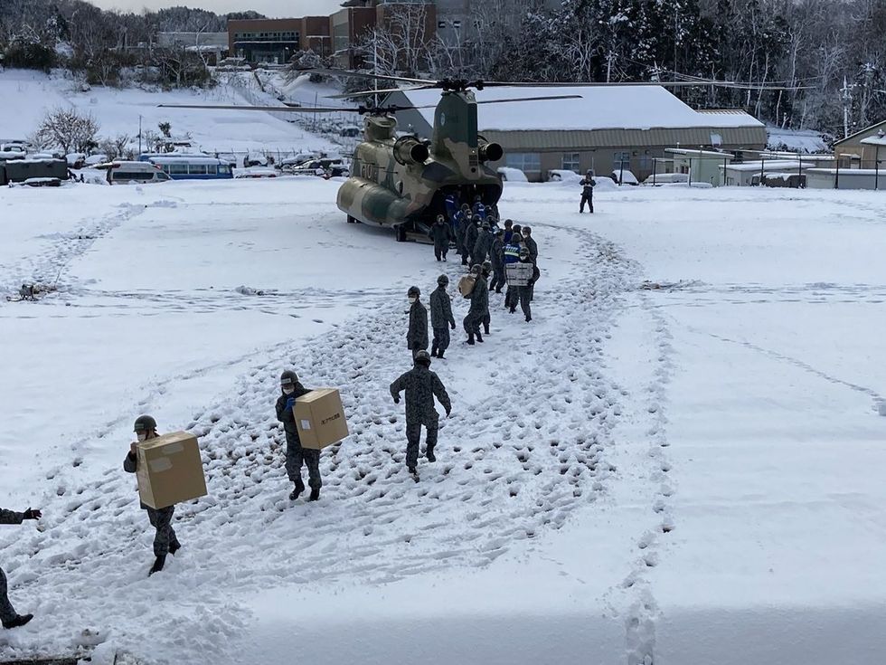a group of people walking in the snow next to a helicopter