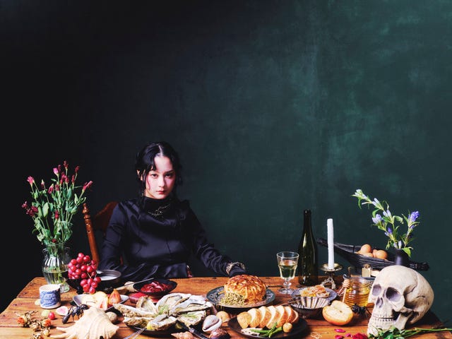 a woman sitting at a table covered with food, flowers, and a skull