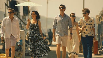 group of people walking along a sunny promenade with a white parasol