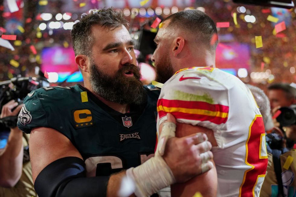 jason kelce, wearing a philadelphia eagles jersey, holds travis kelce by arms and speaks to him in the middle of a large crowd