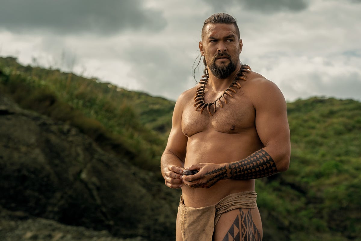 man in a lei standing in front of a large grassy hill
