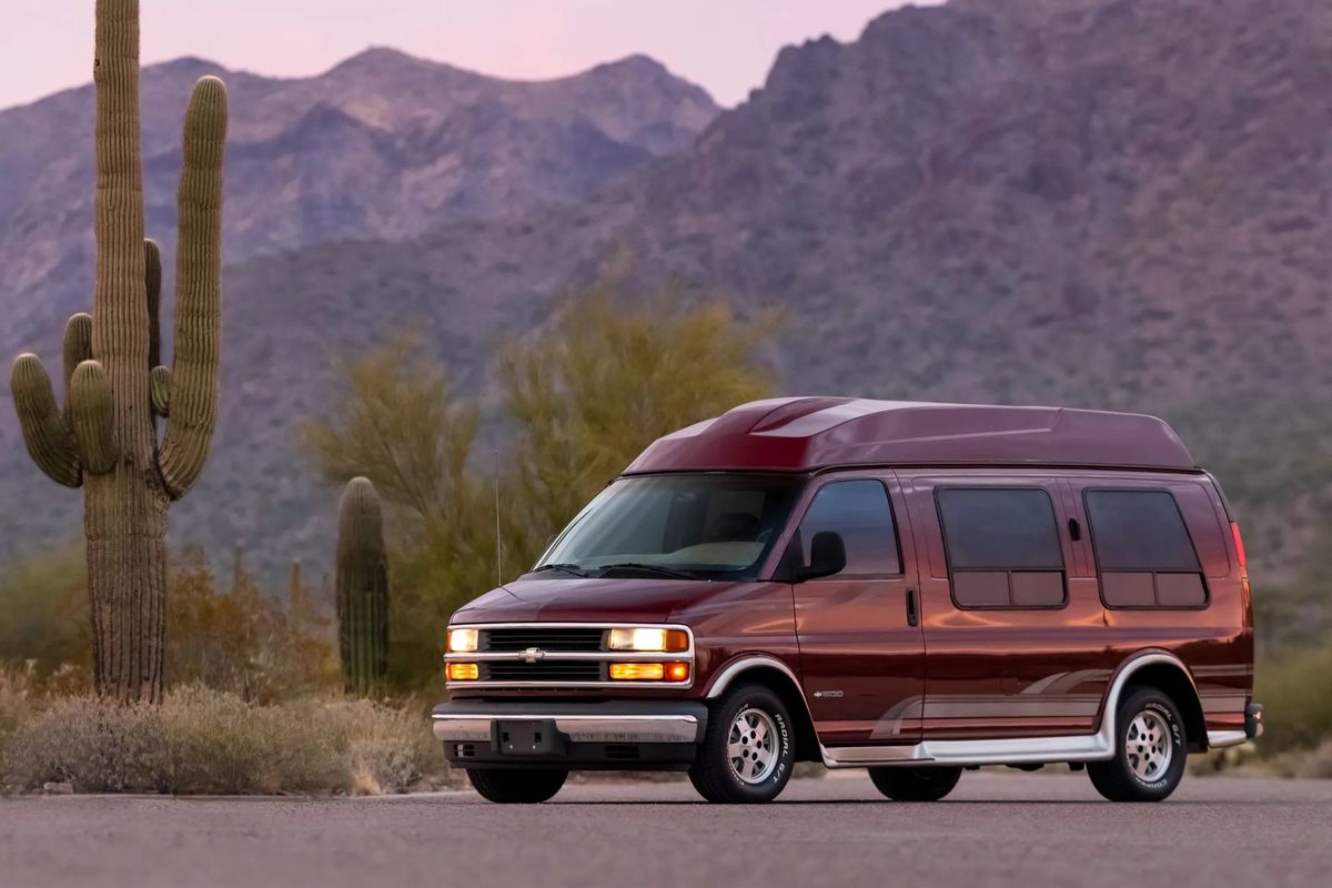 a red chevrolet express conversion van parked in front of a cactus and some mountains
