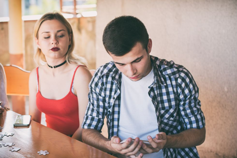 Jealous girlfriend peeking her boyfriend mobile phone while he is reading a message