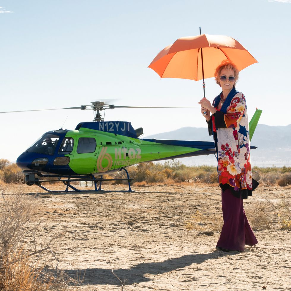 jean smart with a parasol about to board a helicopter
