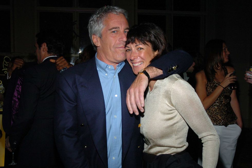 jeffrey epstein and ghislaine maxwell smile at the camera, epstein has an arm around maxwells shoulder, he wears a navy blazer and blue unbuttoned collared shirt, she wears a silver long sleeve top