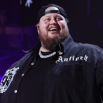 jelly roll holding out his arms and smiling while performing during a concert