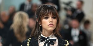 jenna ortega poses on met gala carpet in a blck jacket over a white blouse with a black bow tie and a thick fringe hairstyle