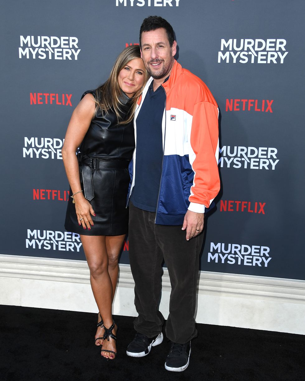 jennifer aniston and adam sandler pose for photos, smiling and standing in front of a black murder mystery movie background
