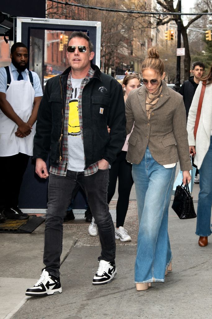 jennifer lopez and husband ben affleck lopez is wearing a brown blazer, blue jeans and white heels affleck is wearing a black jacket and jeans with white and black nike trainers