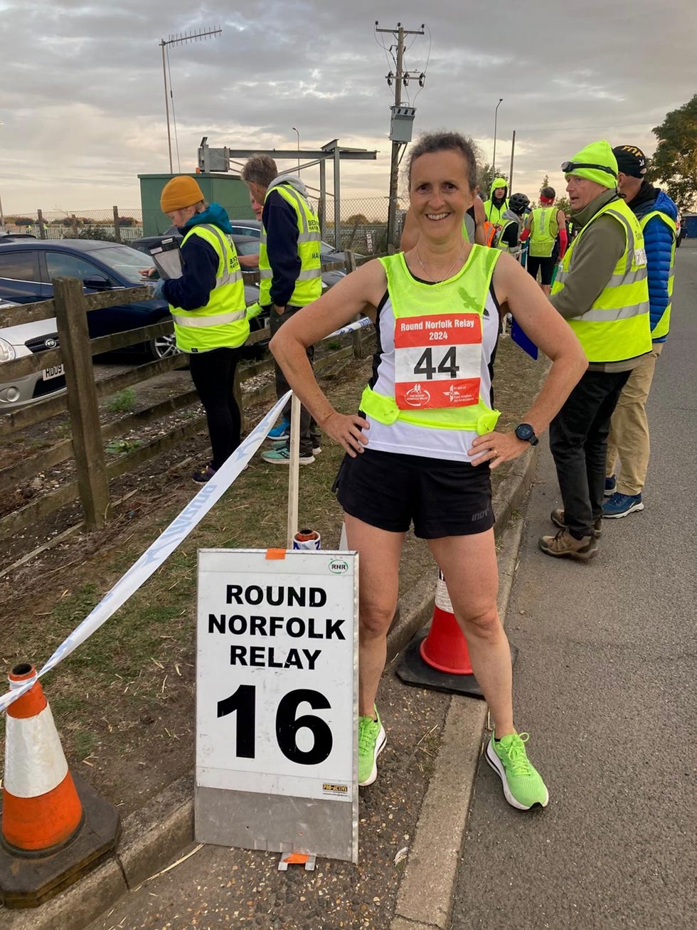 a smiling runner poses beside a race sign