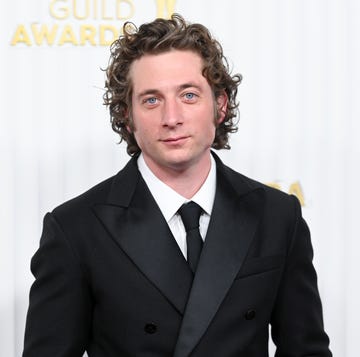 jeremy allen white looks at the camera with a slight smile, he wears a black suit and tie with a white collared shirt