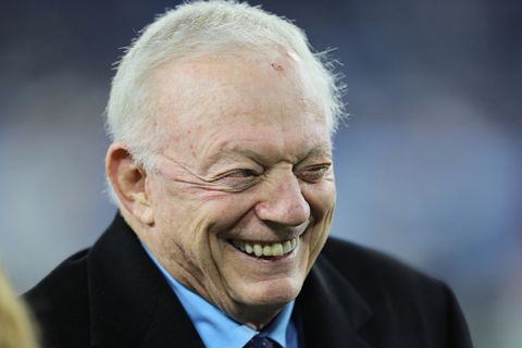 jerry jones, wearing a black coat, blue shirt, and blue tie, laughs and looks off camera