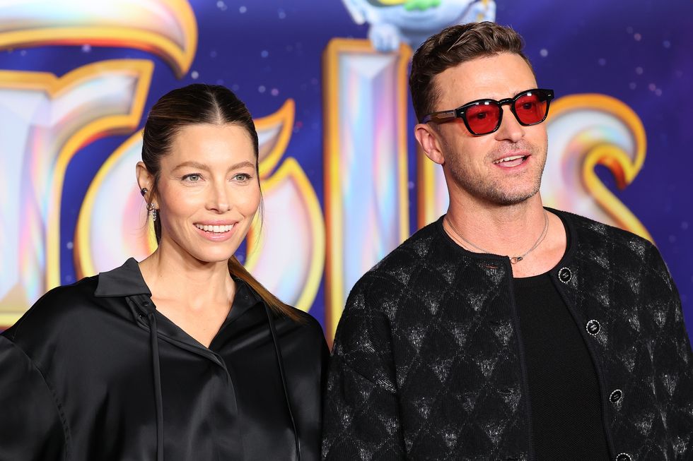 jessica biel and justin timberlake smiling in front of backdrop featuring trolls band together artwork