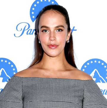 jessica brown findlay poses wearing her hair slicked back in a half ponytail and a structured, checkered puffy sleeved top and trousers coord with matching gloves