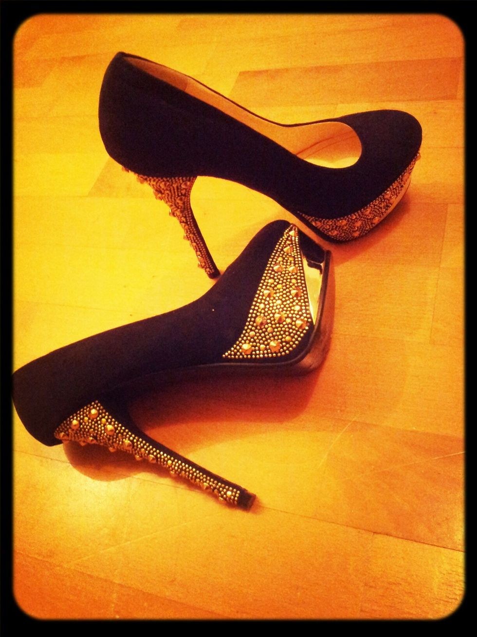 black shoes against a wood floor with the high heels and side of the shoes in gold jewels