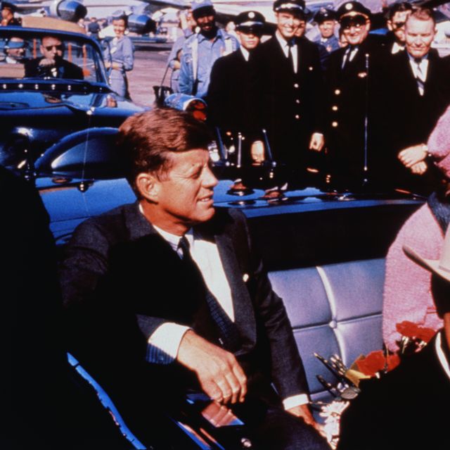 original caption texas governor john connally adjusts his tie foreground as president and mrs kennedy, in a pink outfit, settled in rear seats, prepared for motorcade into city from airport, nov 22 after a few speaking stops, the president was assassinated in the same car