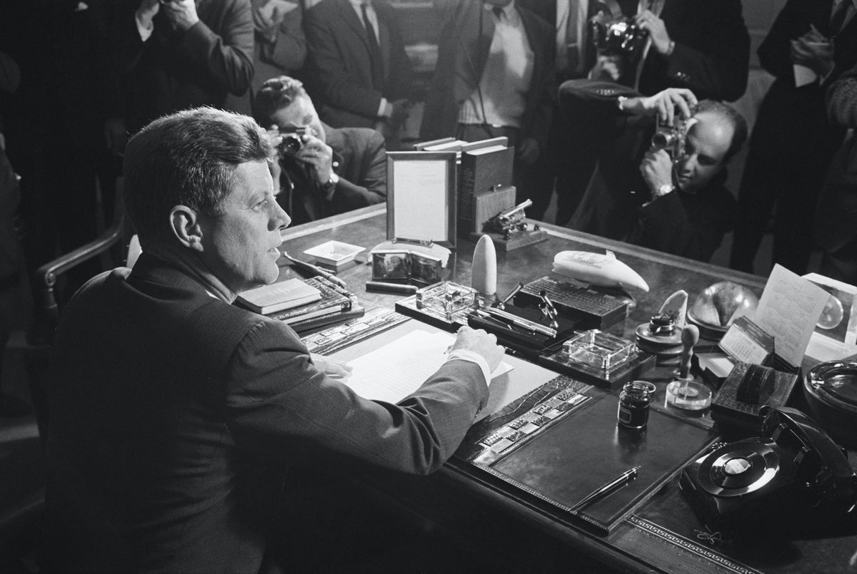 reporters take pictures of president kennedy behind his desk, after signing the arms embargo against cuba the embargo effectively quarantined cuba