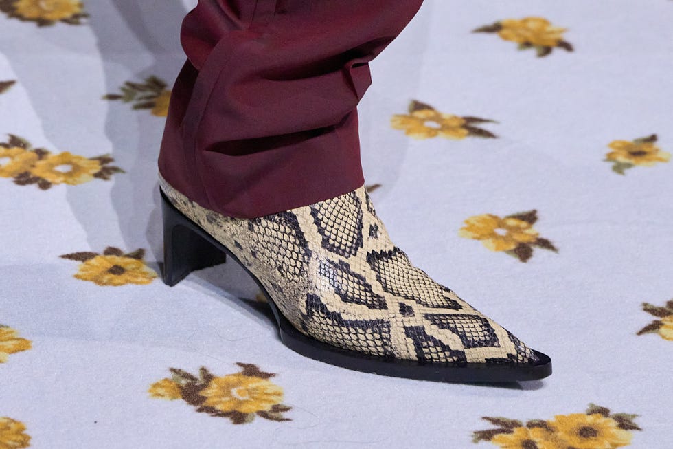 pointed toe ankle boot with a snakeskin pattern and a high heel paired with maroon pants