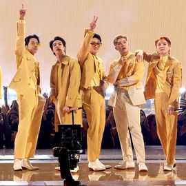 seven young ment stand on a stage and pose, they wear matching and coordinating yellow suits