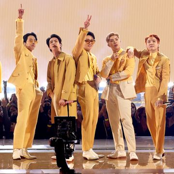 seven young ment stand on a stage and pose, they wear matching and coordinating yellow suits