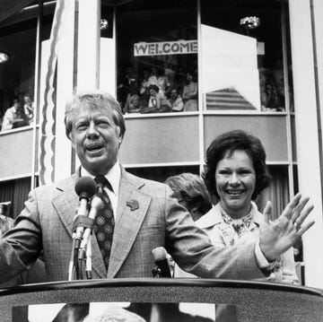 Jimmy Carter jimmy carter wearing a suit and tie and speaking into a microphone at a podium, standing next to his wife rosalynn, with supporters in stands behind him