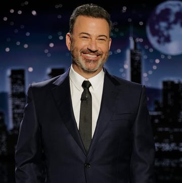 jimmy kimmel smiles at the camera, he wears a navy suit jacket, black tie, and collared white shirt
