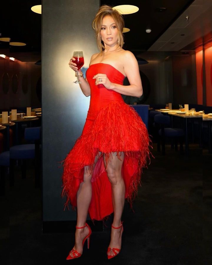 a full body photo of jennifer lopez posing in a red cult gaia dress and holding a cocktail