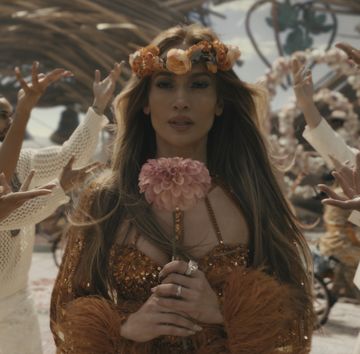 jennifer lopez in an orange gown holding a flower while dancers in white stand behind her