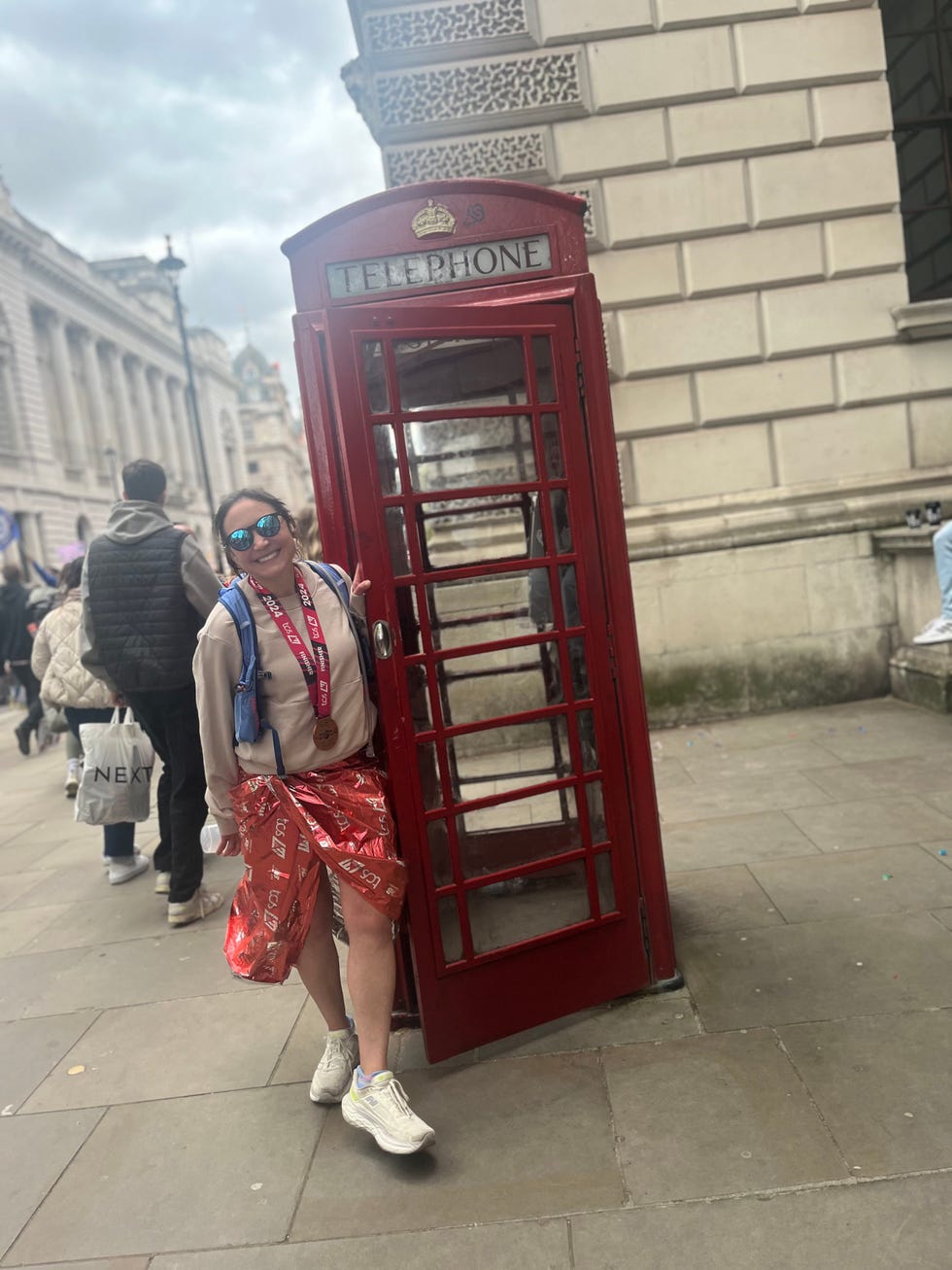 a person in a red outfit stands next to a red telephone booth on a city street