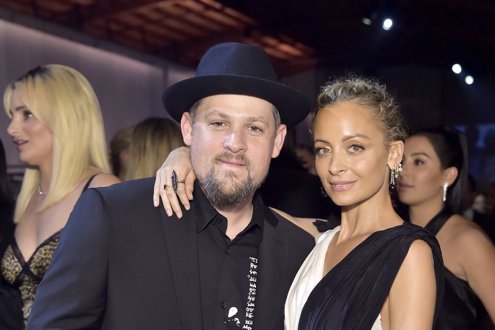 joel madden and nicole richie embrace for a photo, both look at the camera with slight smiles, madden wears an all black outfit with a black hat, richie wears a black and white formal gown and dangling earrings