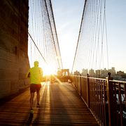 jogger in bright jacket running into the sunset on brooklyn bridge