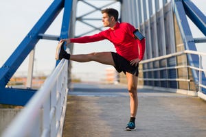 jogger with smartphone in arm pocket stretching his leg