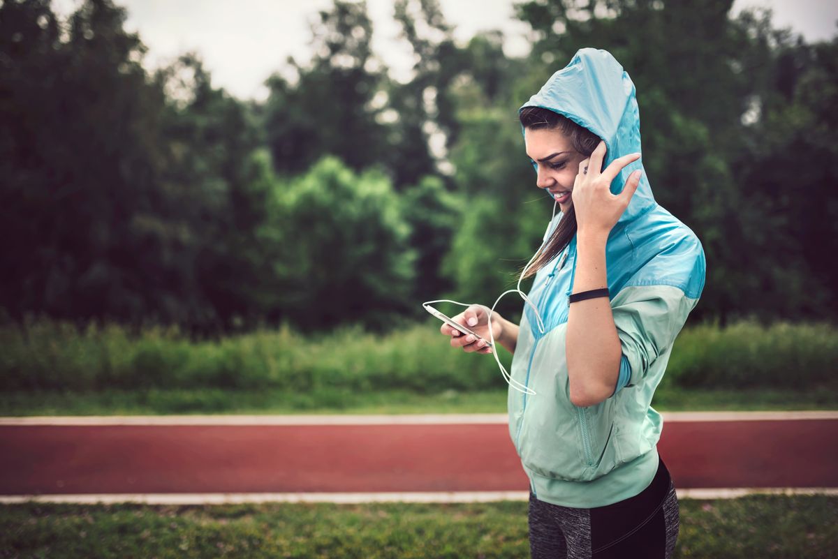 Jogging Girl With Earbuds and Rain Jacket Looking at Cellphone
