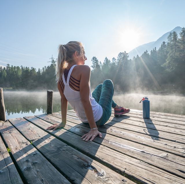 jogging woman relaxing on lake pier at sunrise enjoying freshness from nature