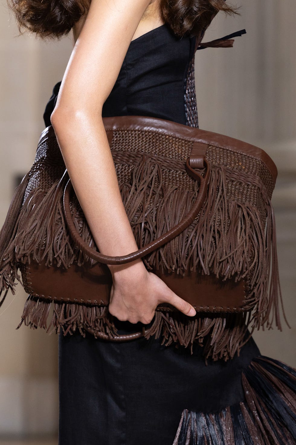 Hand holding a brown fringed bag with a woven texture