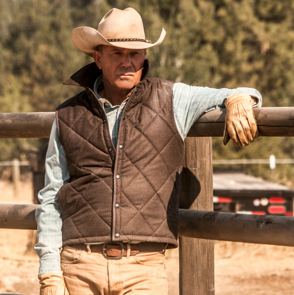 john dutton from yellowstone leaning up against a fence