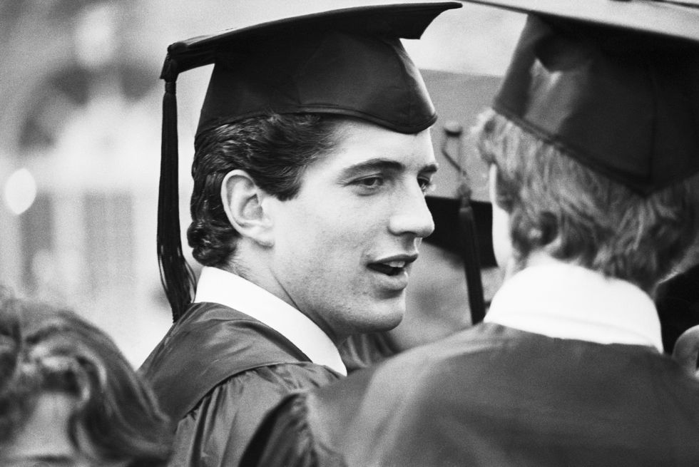 John F. Kennedy Jr., in cap and gown, chats with a classmate at his graduation ceremony at Brown University, where he received a Bachelor of Arts in History.