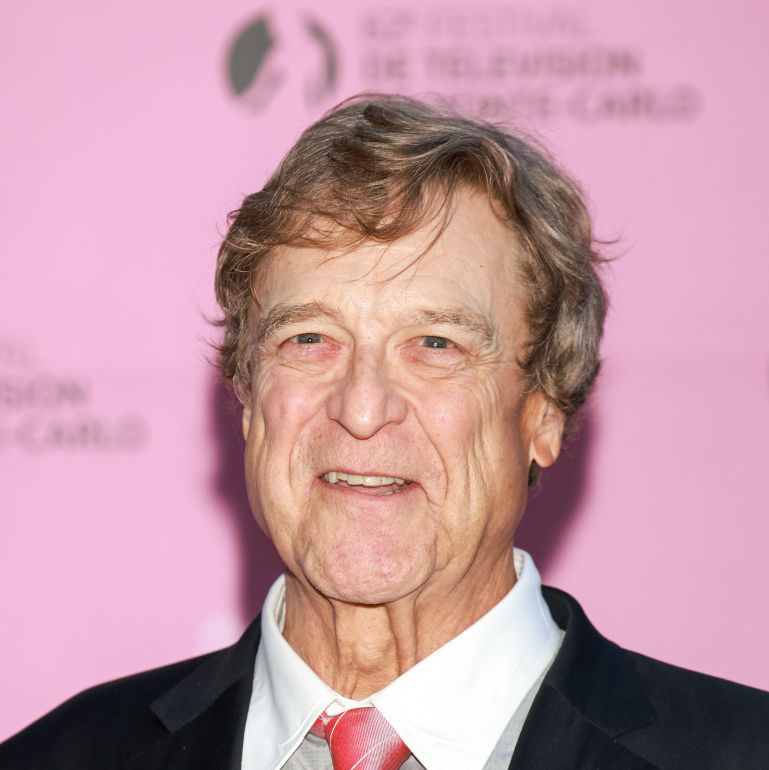 john goodman smiling in front of a pink background