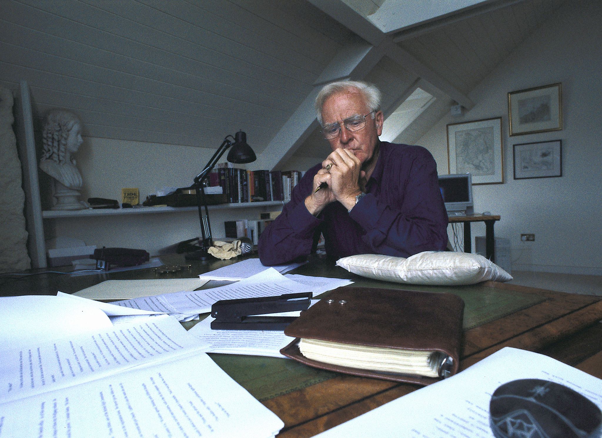 el escritor john le carré, sentado en su escritorio frente a varios manuscritos