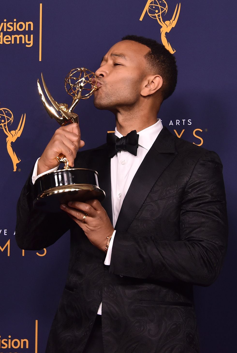 john legend, who is wearing a dark tuxedo, kisses his emmy at microsoft theater in los angeles, california