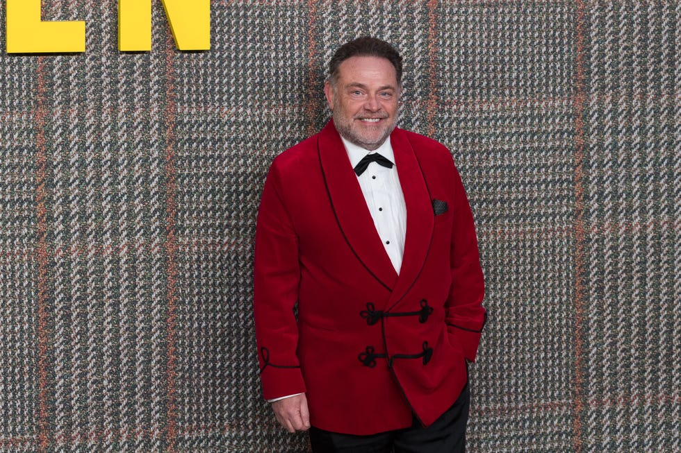 john thomson wearing a red jacket over a white shirt at the gentlemen 2024 premiere event