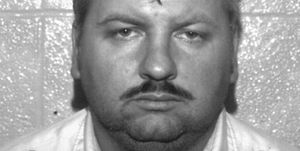a mugshot of john wayne gacy who looks directly at the camera with a neutral expression on his face, below his chin is a black marker that reads "police dept"