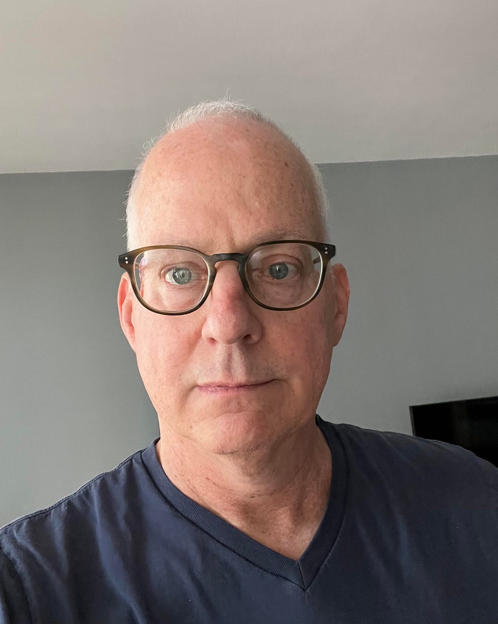 closeup portrait of a man with gray hair and a dark shirt in a room