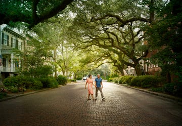 a man and woman walking down a street with trees and buildings