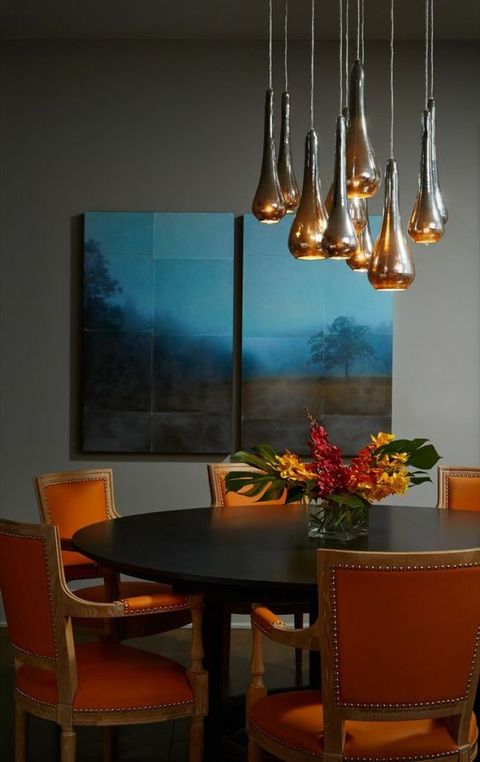 dark gray wall in a dining room with a black table and orange chairs and blue and gray wall art that's abstract