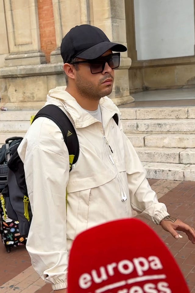 A person wearing a white jacket and a cap standing near steps with a microphone logo in the foreground